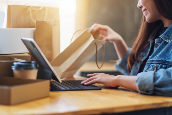 eine junge Frau benutzt einen Tablet-PC zum Online-Shopping und öffnet Einkaufstaschen