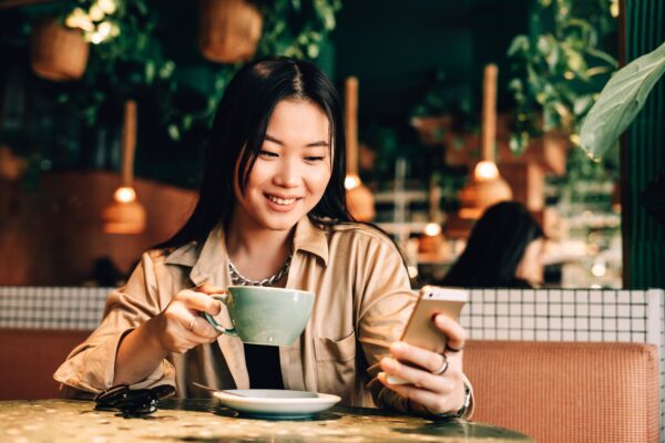 Chica asiática hablando por teléfono y tomando café en una cafetería