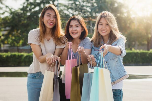 Asian woman shopping in an outdoor market with shopping bags in their hands.