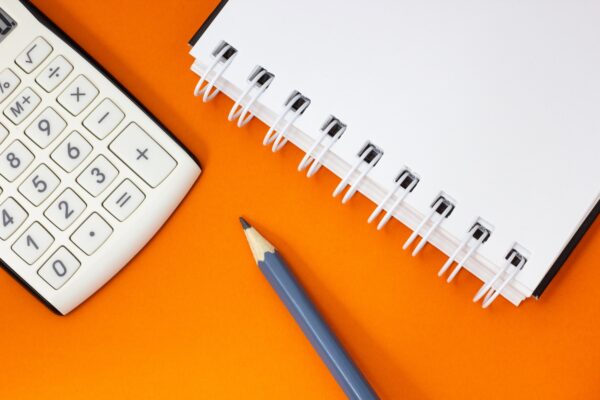 Calculator, notebook and pencil on orange background