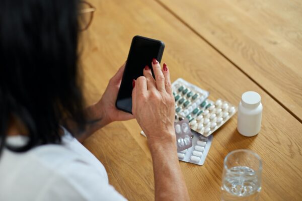 Ältere Frau, die ein Mobiltelefon benutzt und zu Hause online Medizinpillen bestellt