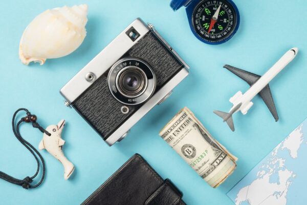 Concepto de viaje desde arriba con cámara retro, brújula, dinero, mapa, concha marina sobre fondo azul.