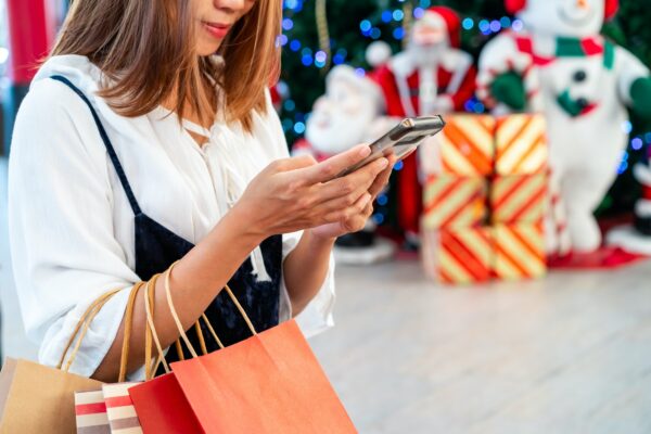 Mujer joven con bolsas de la compra usando el teléfono en tiendas decoradas y centros comerciales