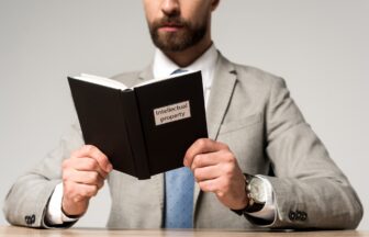 cropped view of businessman reading juridical book with intellectual property title isolated on grey