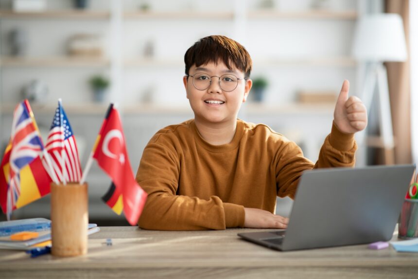 Cheerful chinese boy with laptop and foreign flags